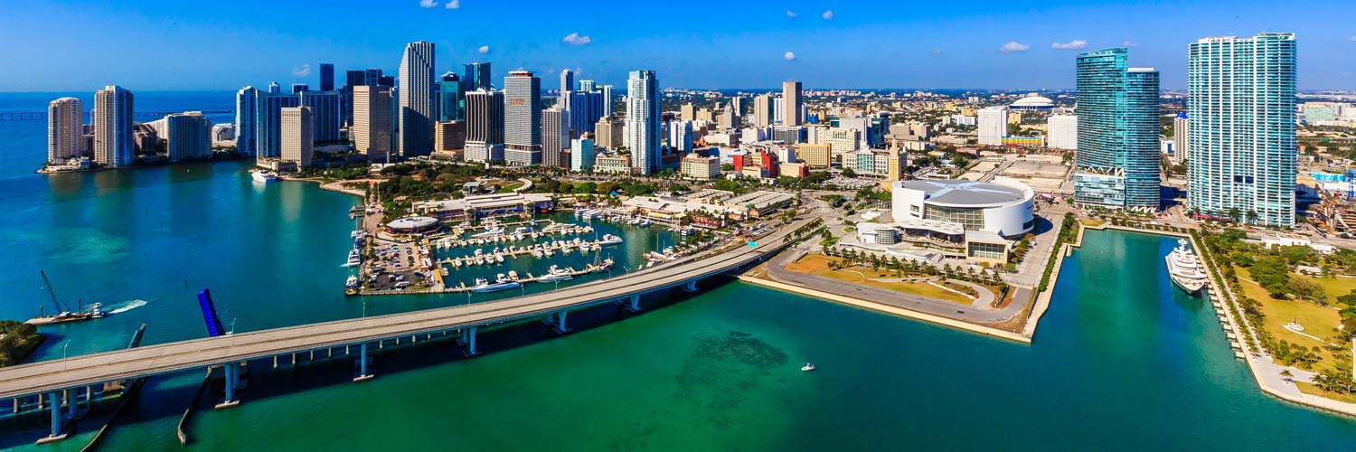 Aerial helicopter view of Downtown Miami, Florida, featuring Biscayne Bay, waterfront marinas, modern skyscrapers, and the Miami skyline.