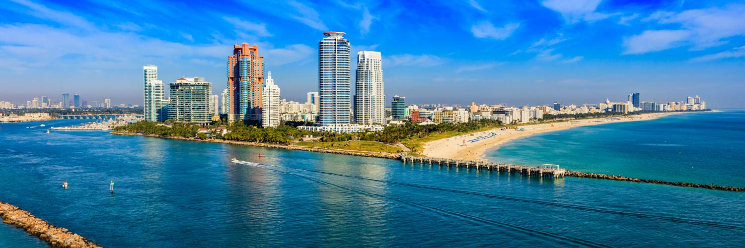 Aerial helicopter view of South Pointe Park and South Beach in Miami Beach, Florida, featuring luxury oceanfront condominiums, white sandy beaches, and turquoise Atlantic waters.